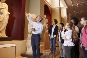 Pupils And Teacher On School Field Trip To Museum With Guide